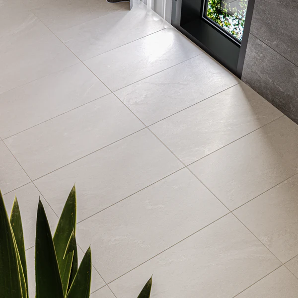 Large square beige porcelain floor tile with a matte, stone-look finish in a bright modern space with a plant. Etna Wall & Floor Tile.