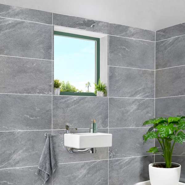 Medium grey large format porcelain tile with a stone/slate look on a modern bathroom wall around a small sink and window. Etna Wall & Floor Tile.
