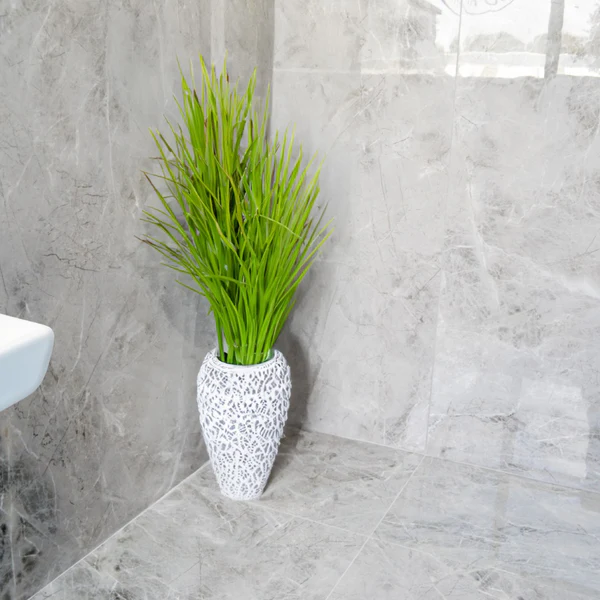 Olympia Pearl wall and floor tiles in a modern bathroom, featuring grey marble-look porcelain and a decorative plant.