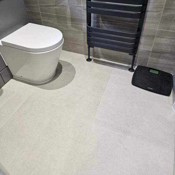 Light grey/off-white Stonetech Wall & Floor Tile with a subtle stone look on a bathroom floor, beside a toilet and dark wall tiles.
