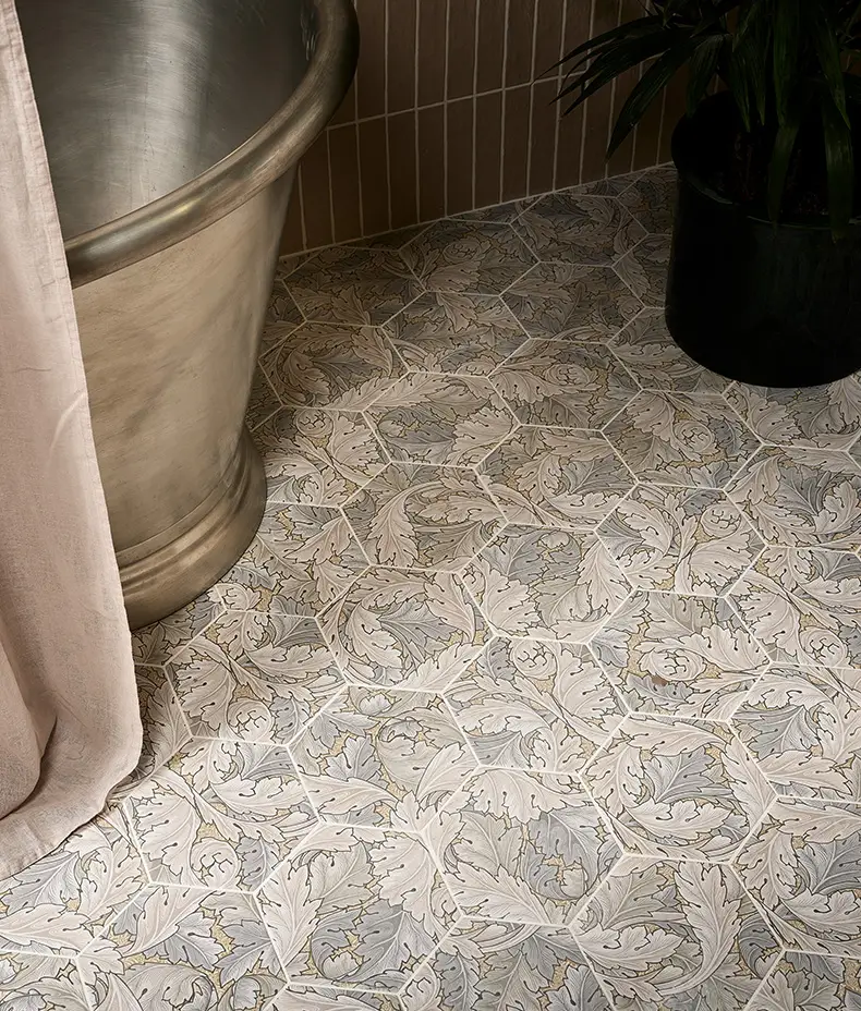 Folly Porcelain Sand Matt 20x23cm hexagonal tiles covering a floor, featuring a repeating sand-colored leaf pattern next to a metal tub.