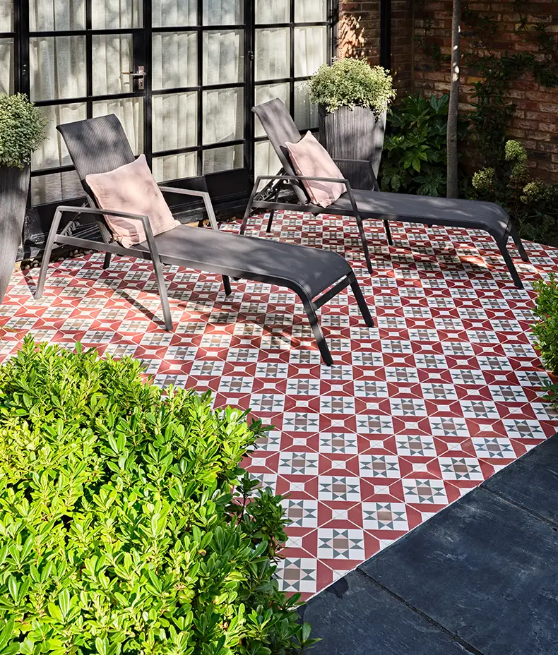 PORTARE Brompton Clarence 20x20cm outdoor tiles with a red, white, and grey geometric star pattern on a patio with sun loungers and greenery.